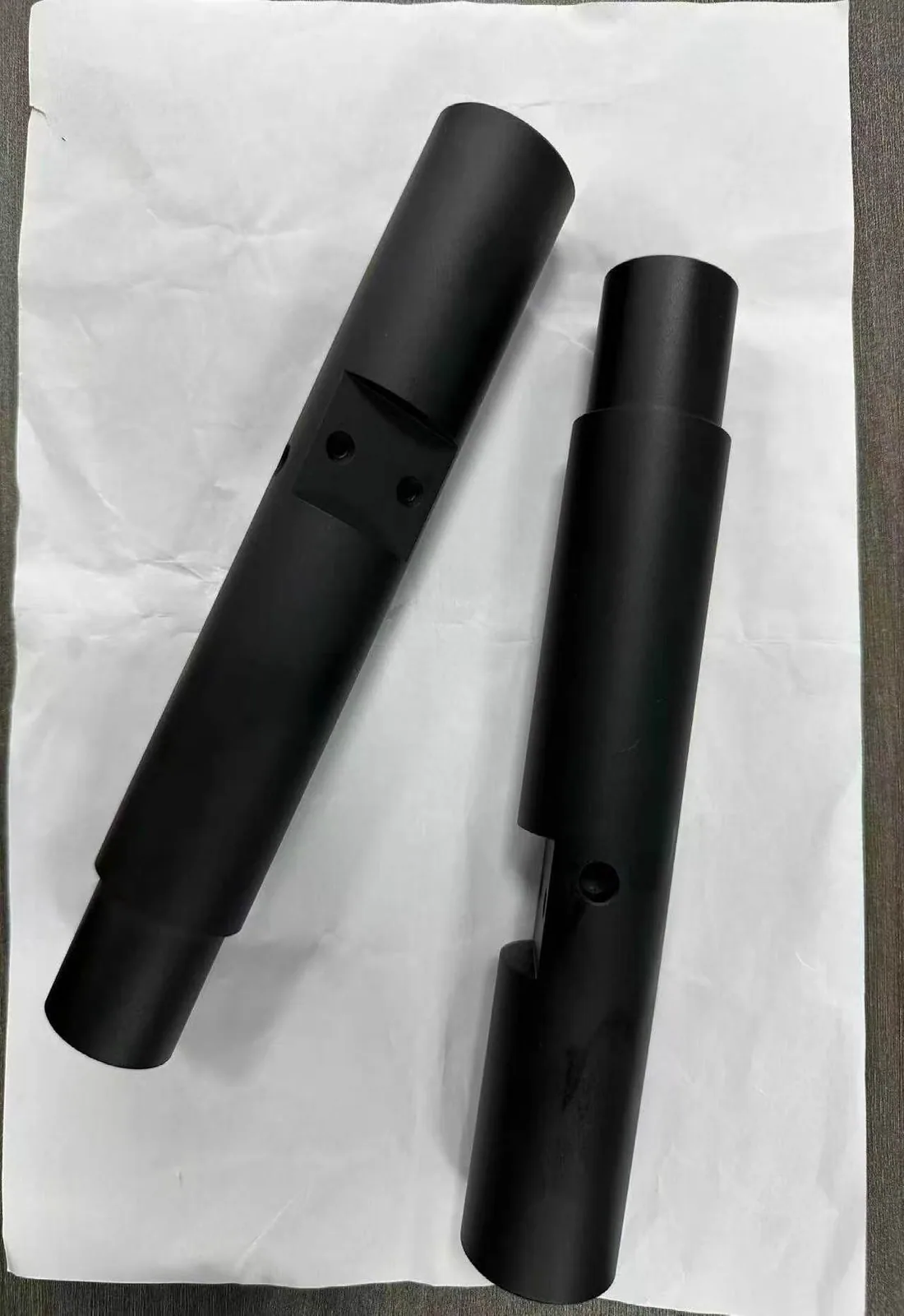 Long dark cylindrical components with stepped sections, holes and slots